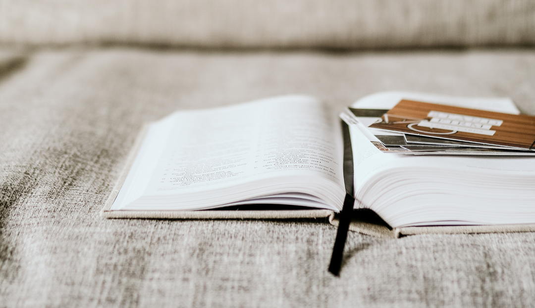 An open bible on a gray couch with some verse cards resting on the pages