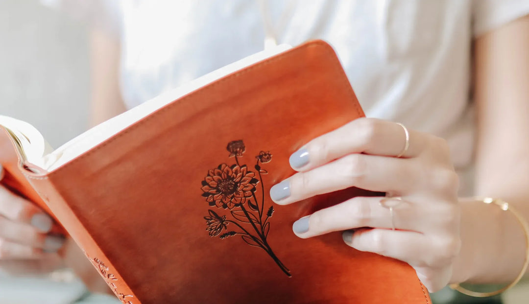 A woman reading a leather bible that has an engraved flower on the cover