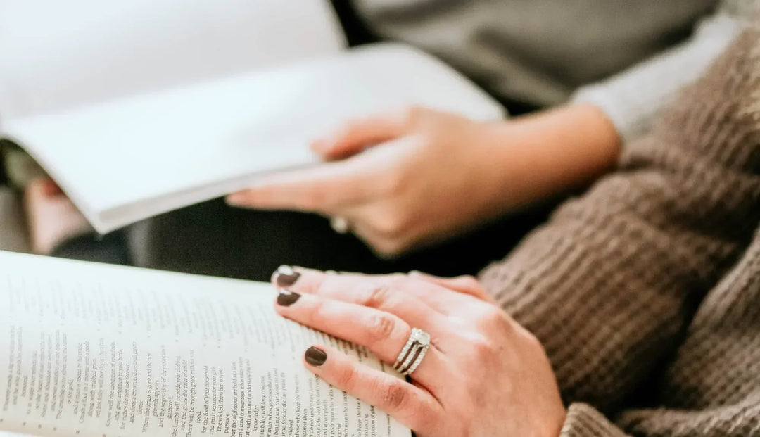 Two women holding open bibles sitting next to each other. The closer woman has her hand resting on the bible page