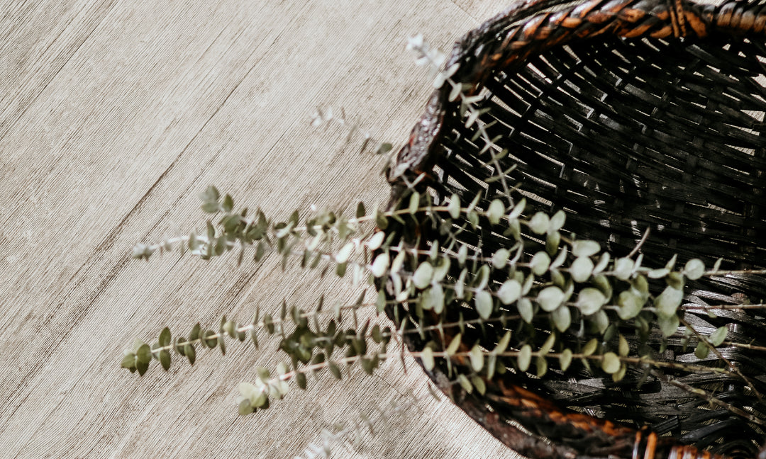 Basket full of eucalyptus on a wooden floor.