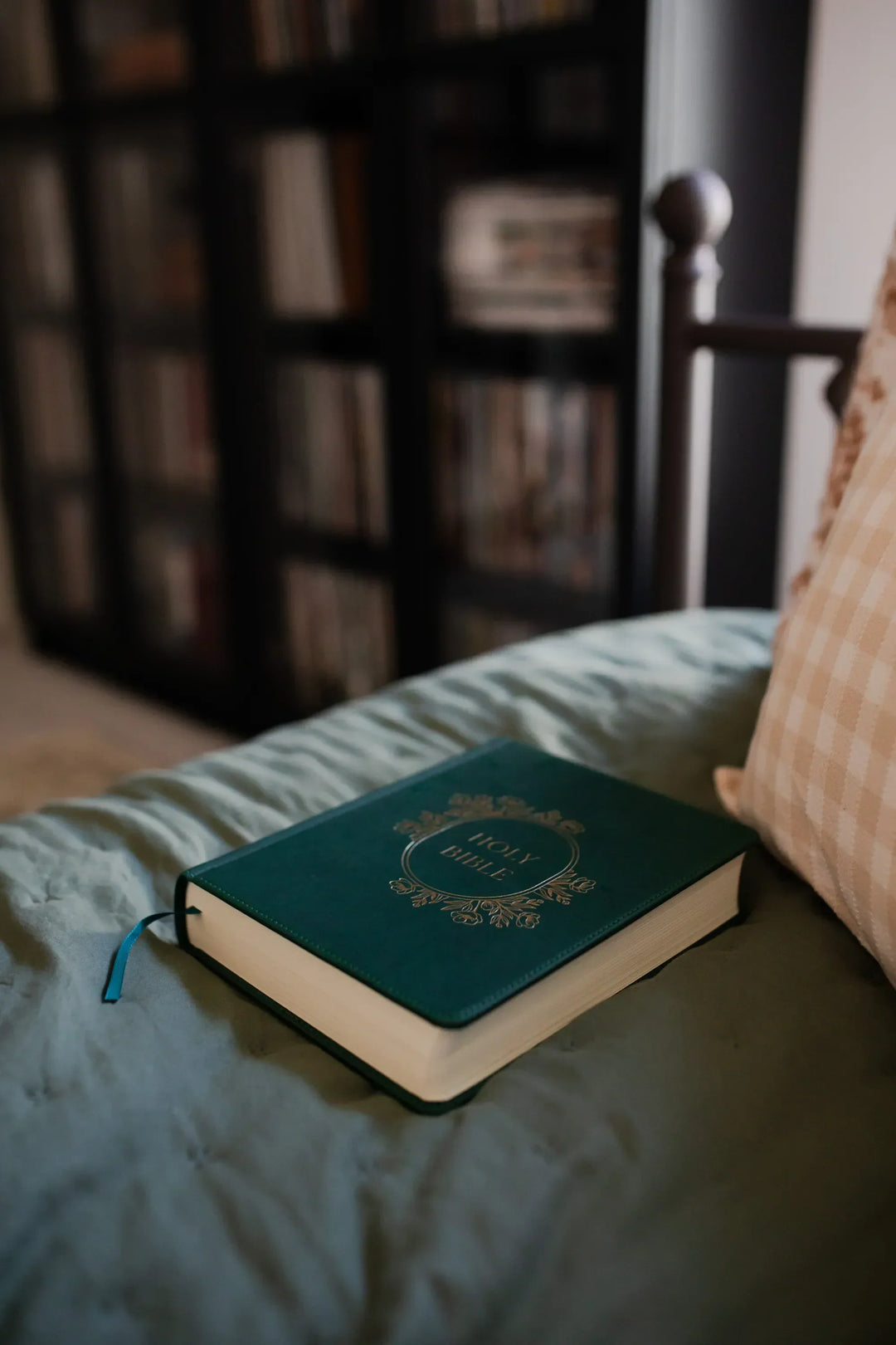 A Dark Green Bible with Gold etching on a plush blanket with a bookshelf full of books in the background