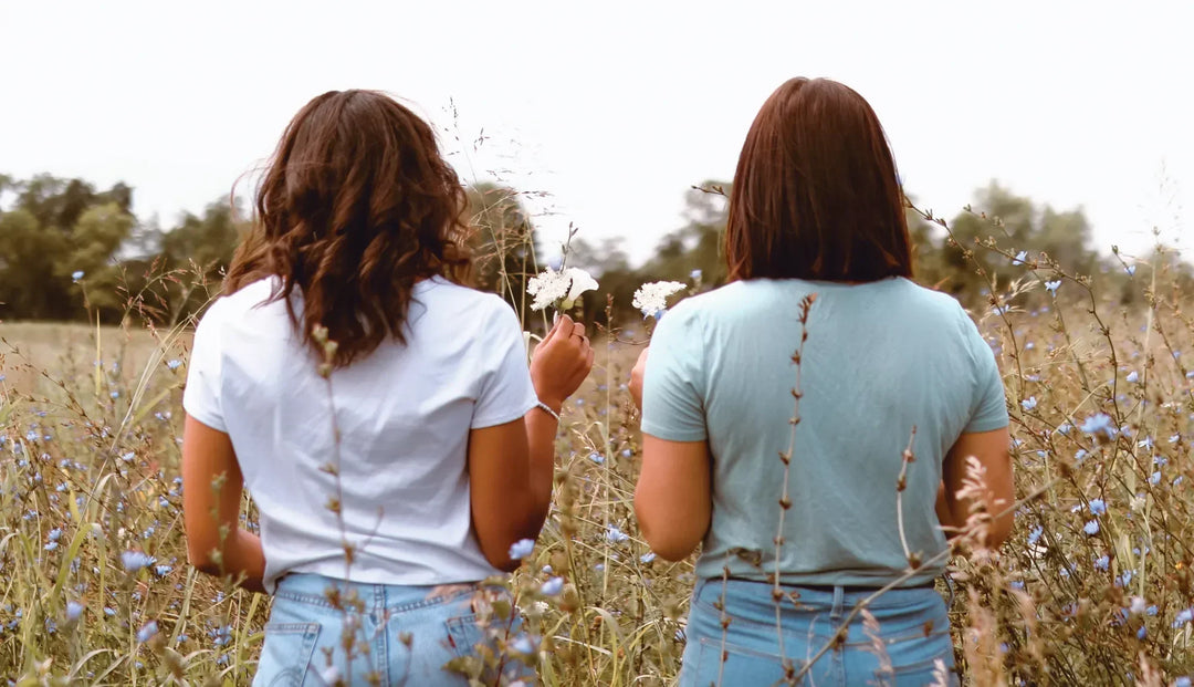 Two women with their backs facing the camera in an open flower field