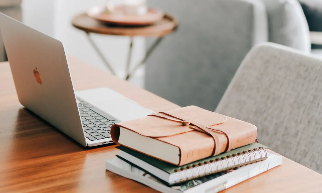 A leather bible next to a laptop on a brown wooden desk