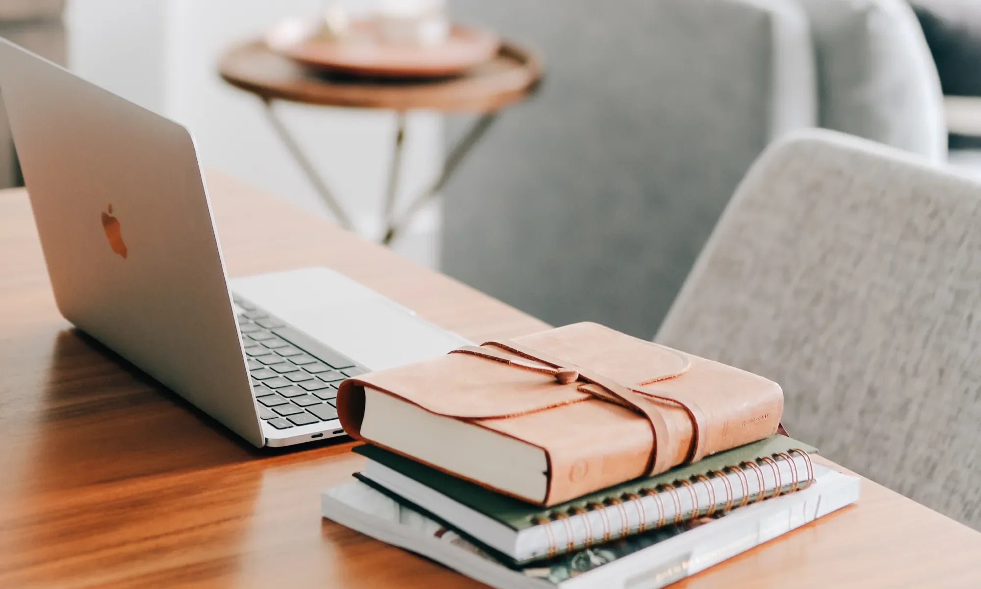 A leather wrapped bible on a spiral study and next to an open apple laptop on a polished wooden desk