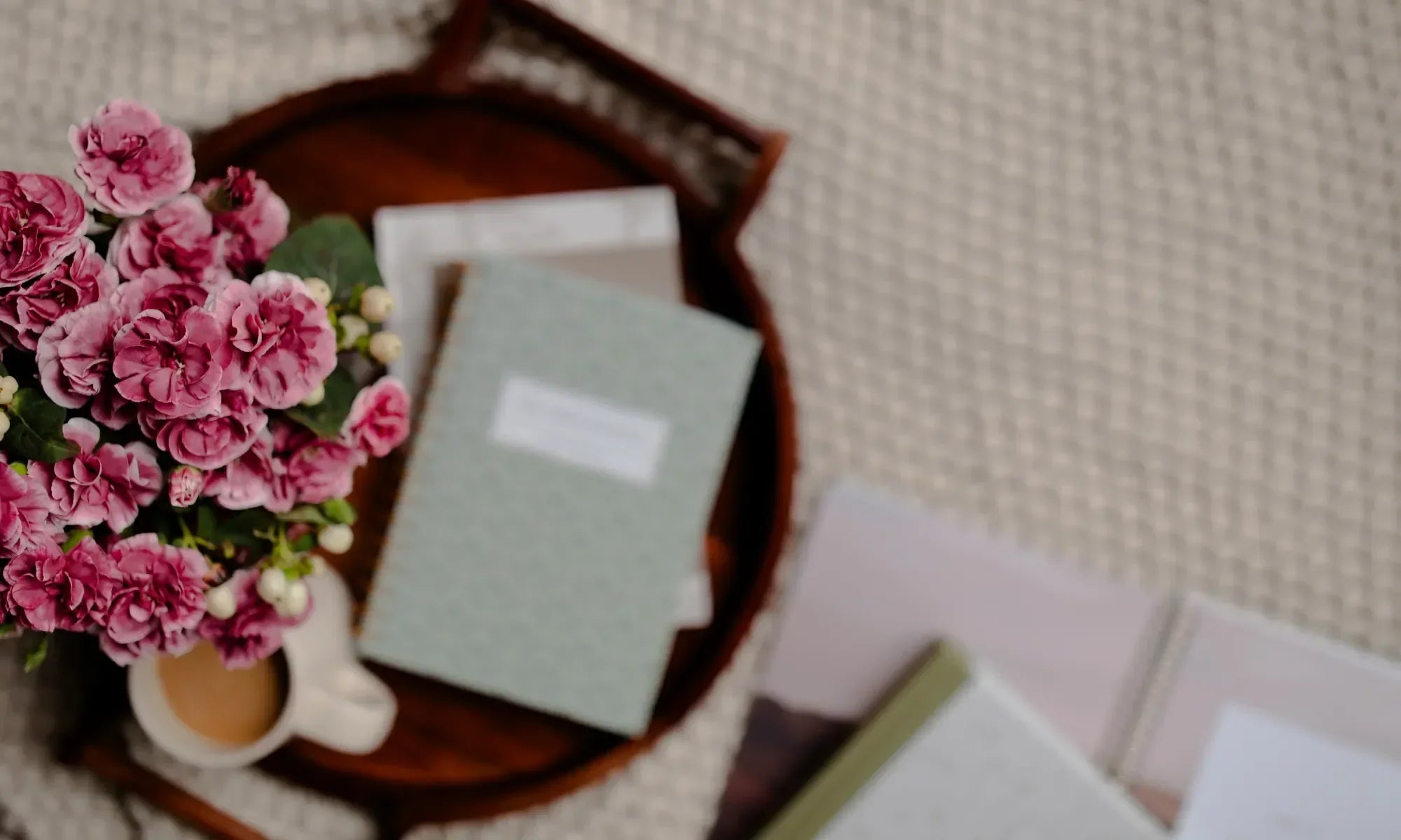 Pink flowers next to a white coffee cup and an abide journal on a wooden tray