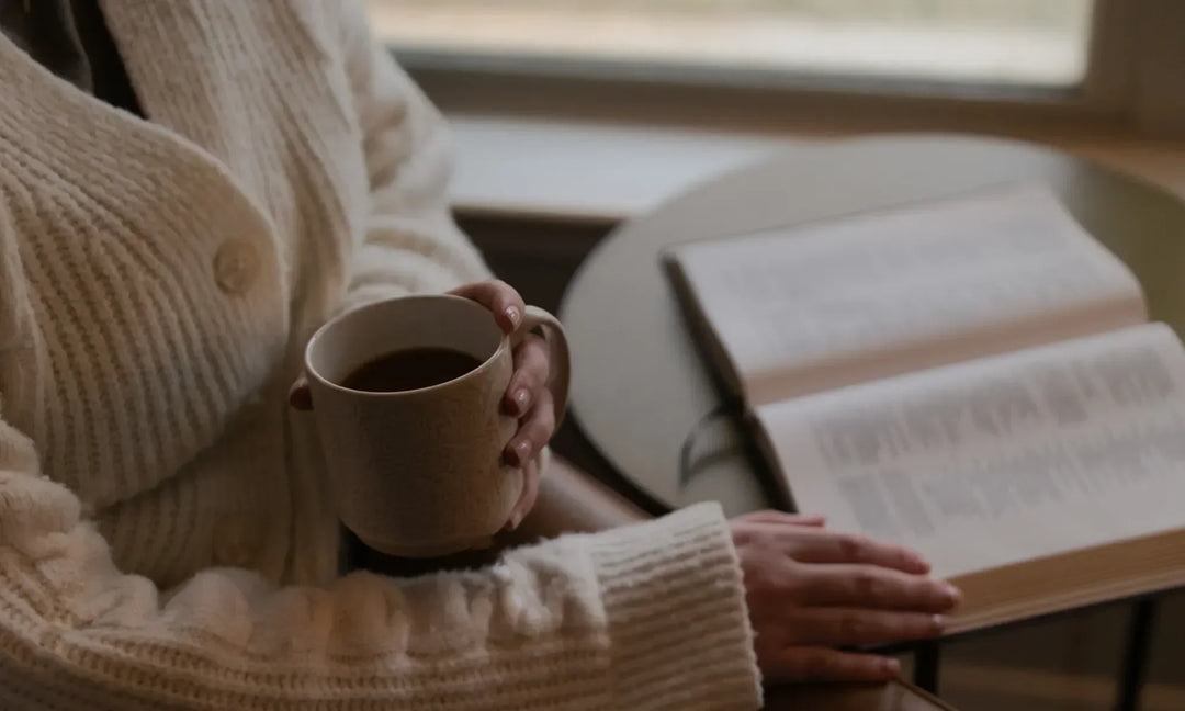 Woman holding a coffee cup while reading an open bible