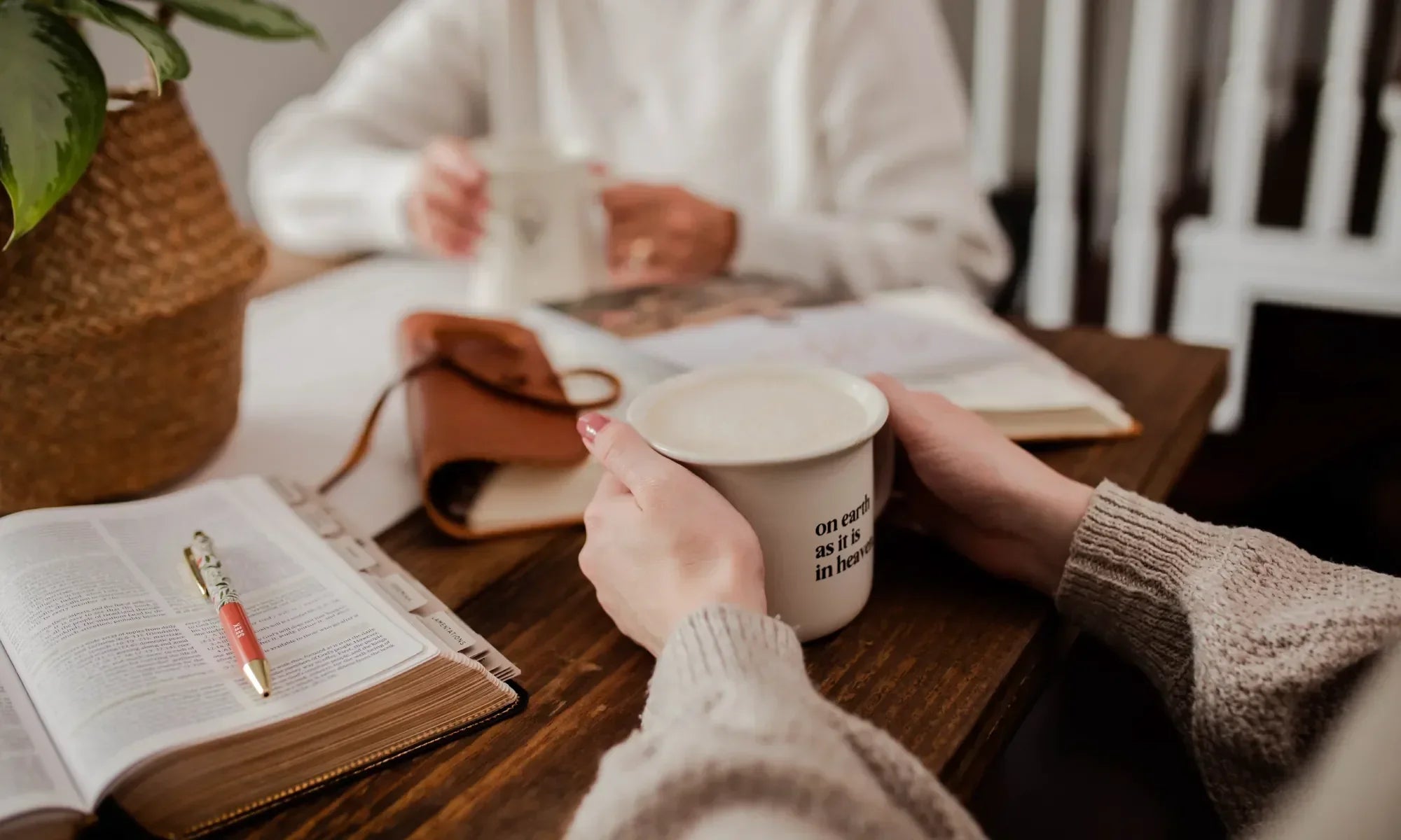 A woman holding a coffee cup next to another woman with various products on the table