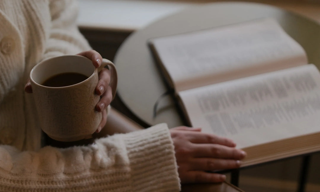 A woman holding a coffee cup reading a bible on a circular toped table