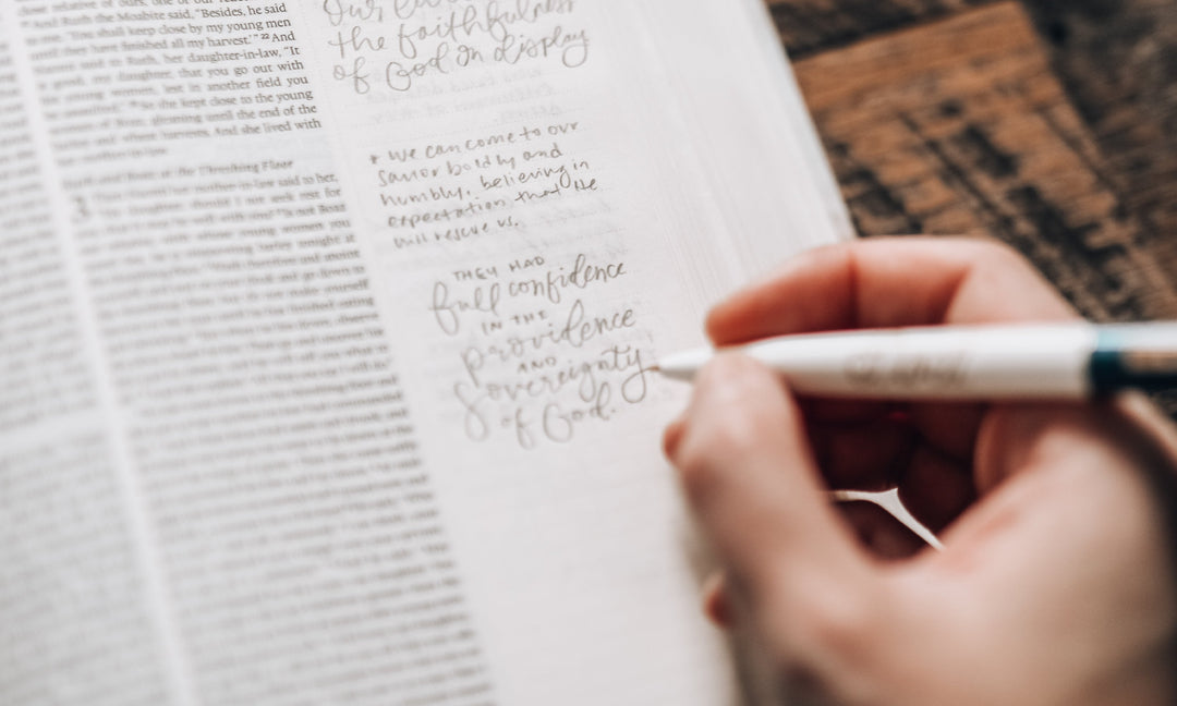 A person's hand writing notes on the side of the bible with a Daily Grace Pen