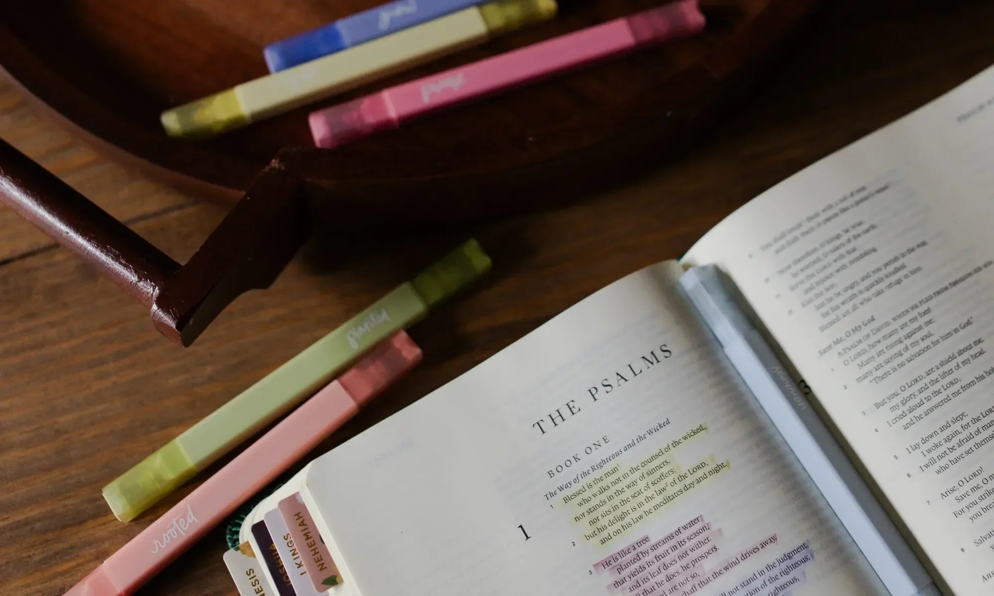 Multiple Daily Grace Highlighters near an open bible on a wooden desk