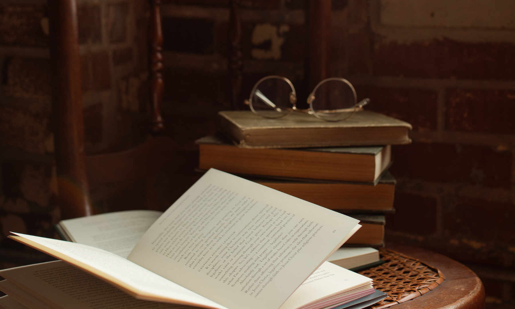 Multiple books stacked with a pair of sunglasses on it near an open book