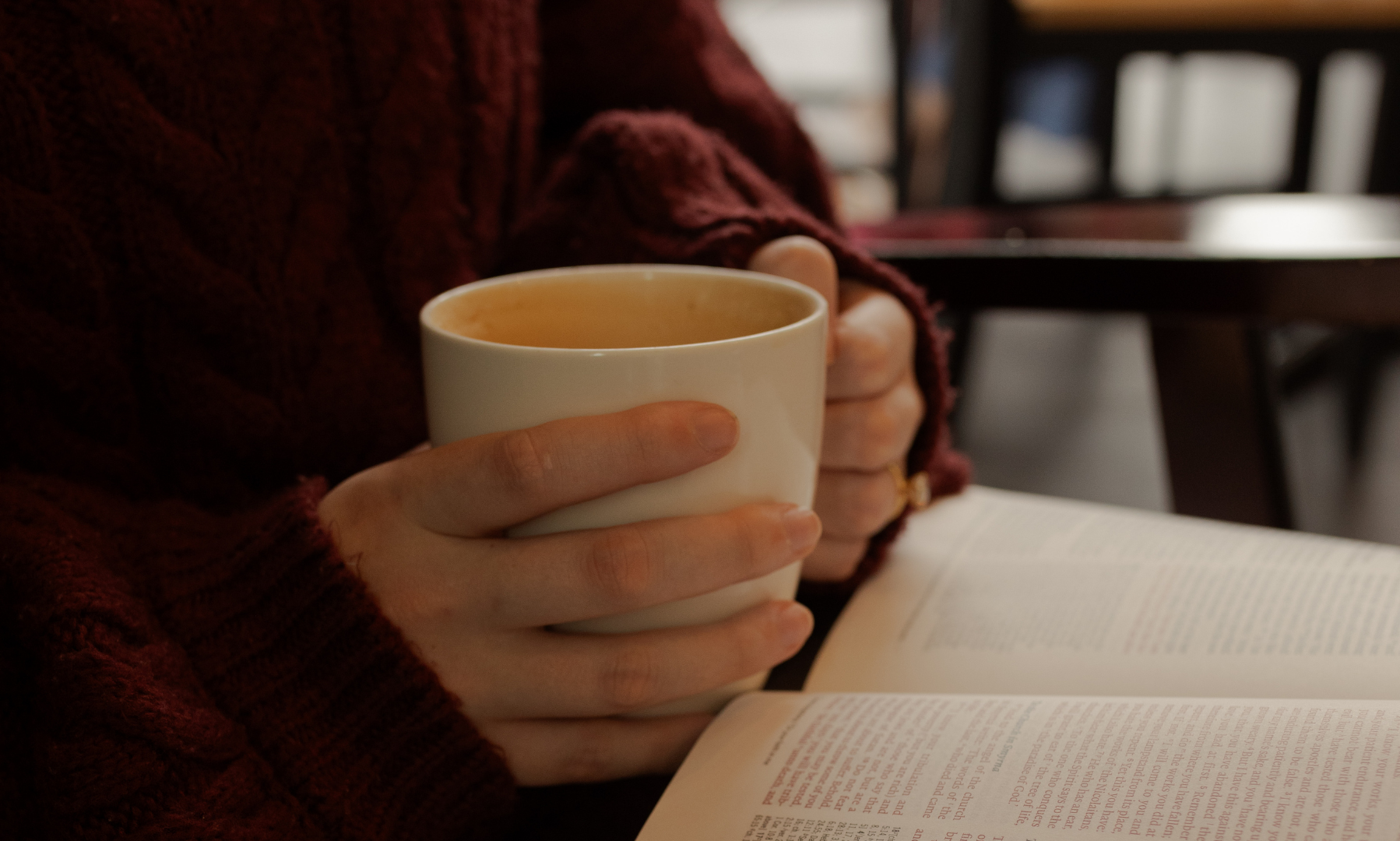 A woman holding a coffee cup with an open bible