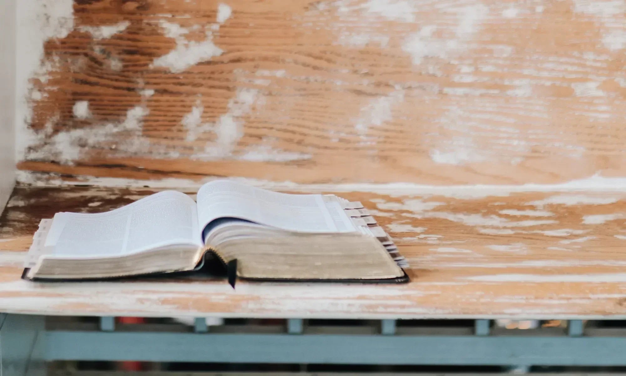 An open bible on a wooden desk with blue table legs