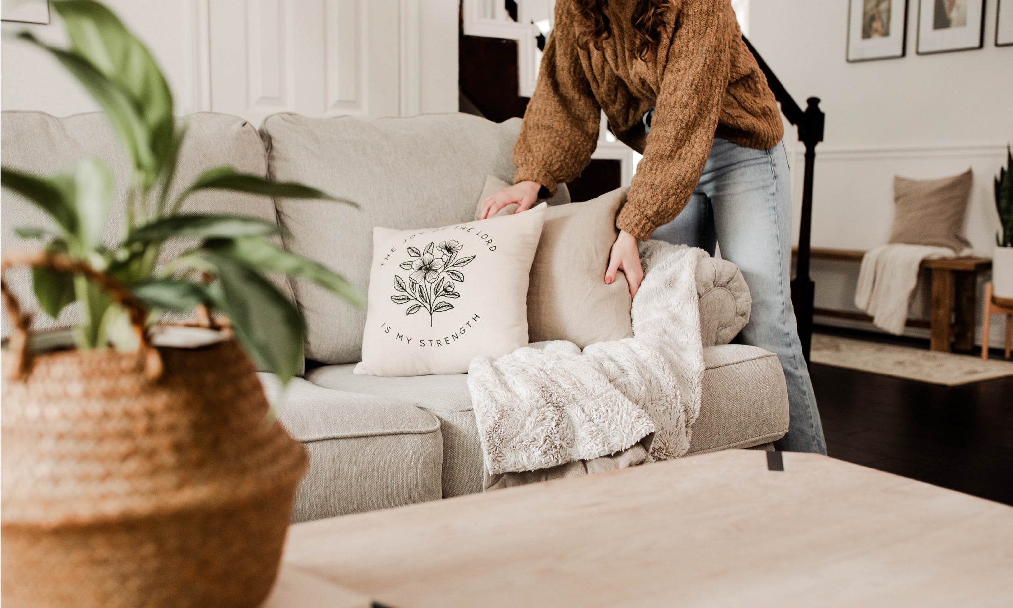 A couch and woman adjusting the pillows in her home.