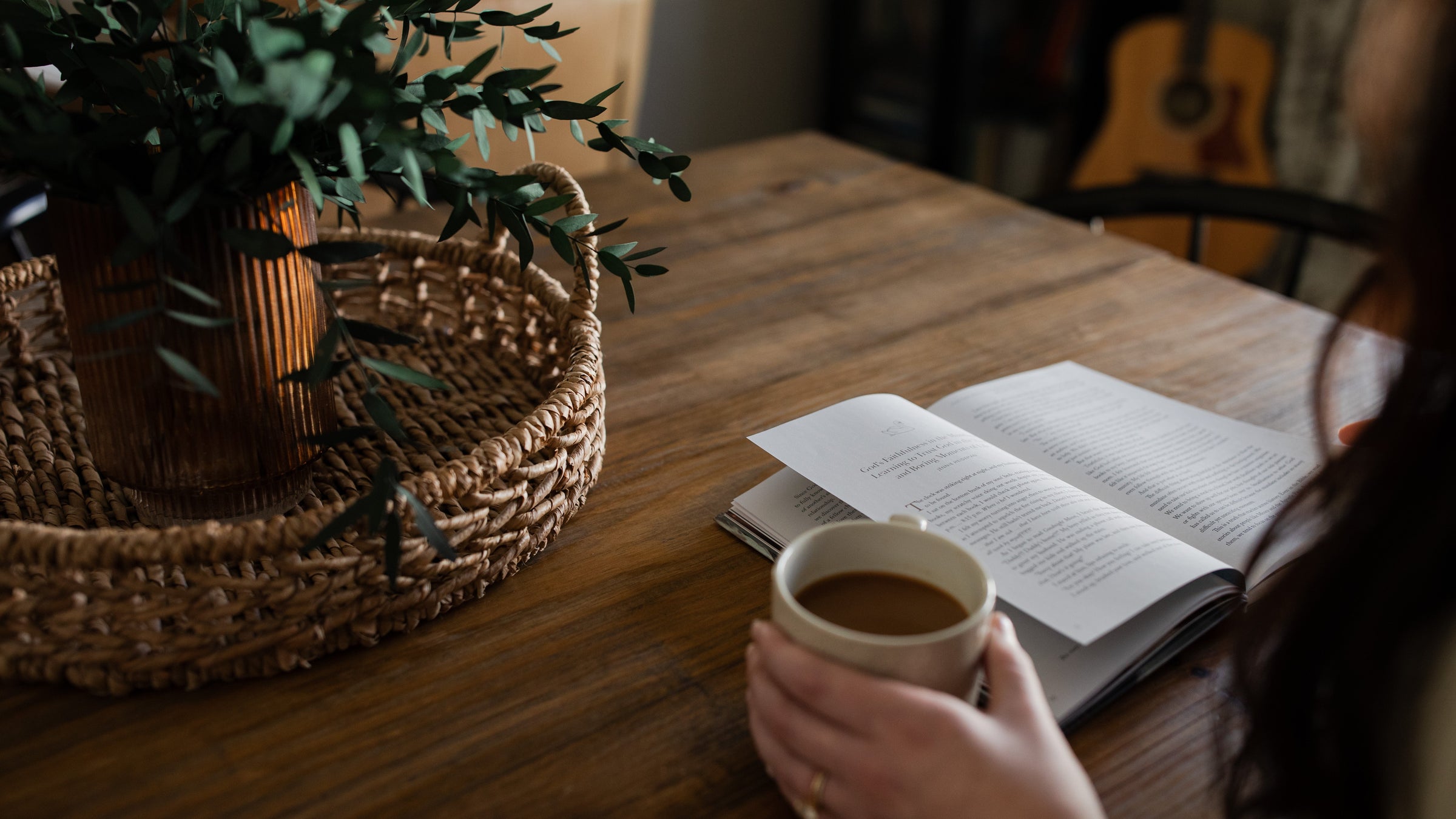 Woman reading a Bible study on a table with a coffee cup next to a basket in a woven basket