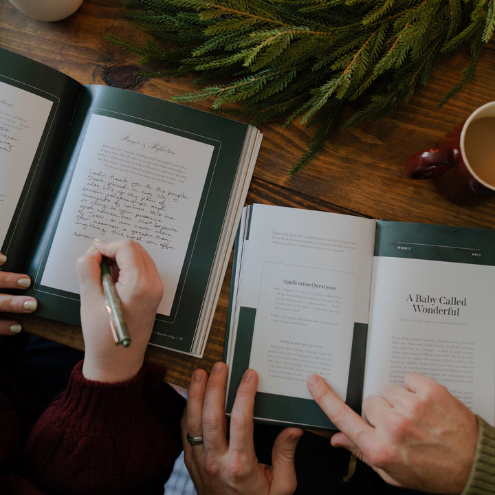 The Awakening Wonder Woman and Mens study open side by side on a wooden table with some greenery and coffee cups nearby; A woman is writing in one study while the man is pointing to one of the application questions in his study