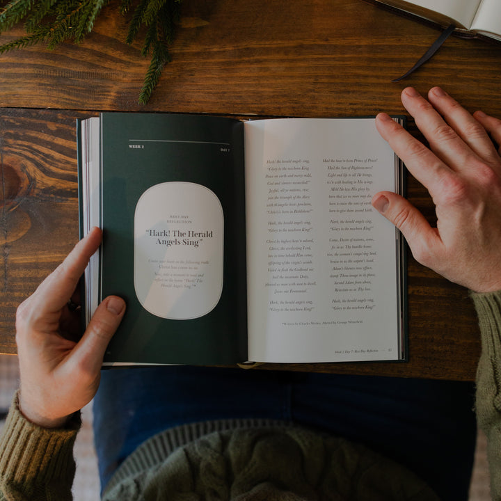 A man's hands holding the Awakening Wonder study open to the Week 2 Day 7 reflection page