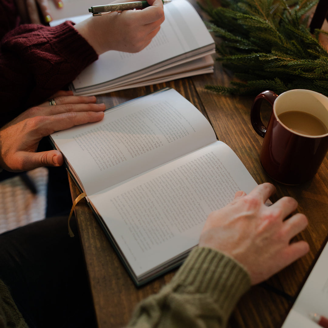 A man holding open the Awakening Wonder study open with a coffee cup next to him and a woman writing in a study