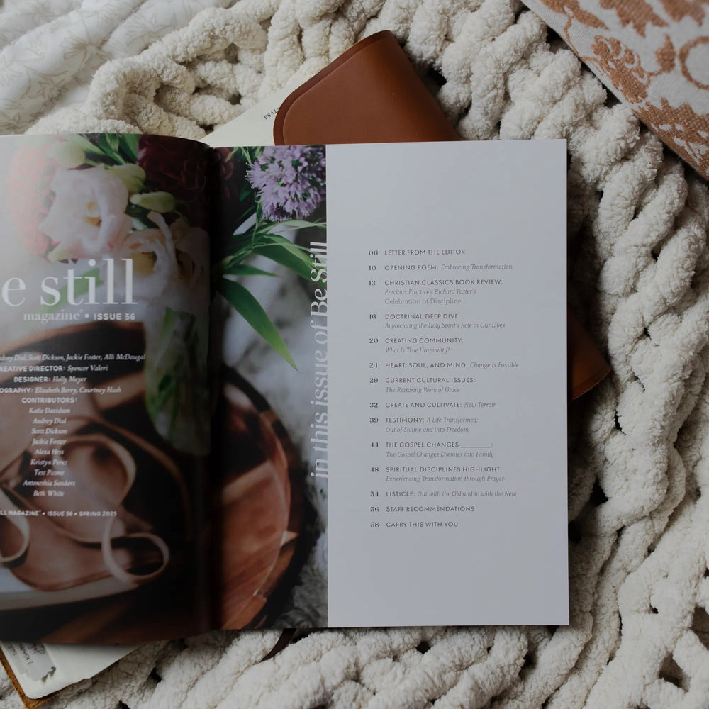 Be Still Issue 36 Magazine opened to the table of contents laying on an open bible on a white knitted blanket