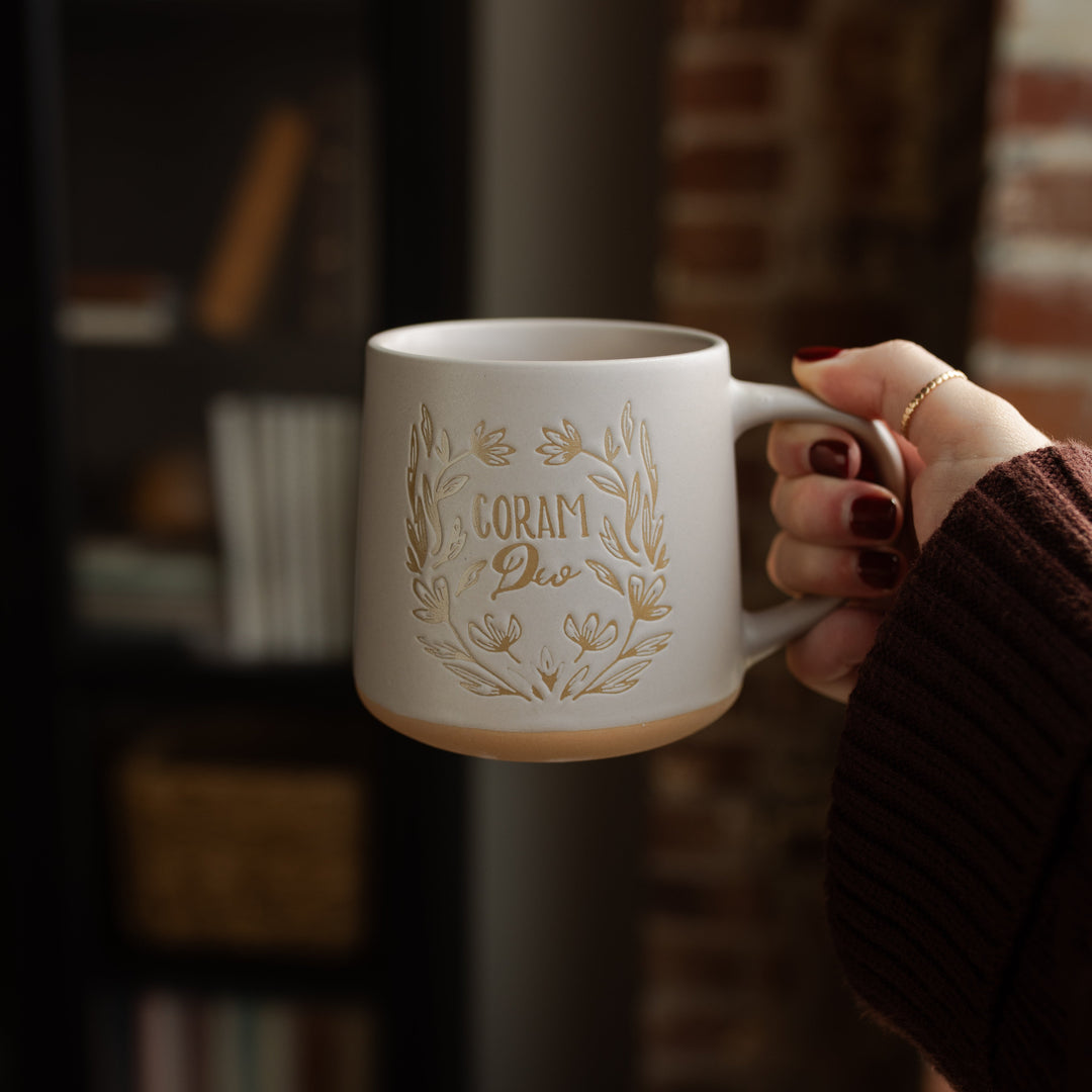 A woman holding a coffee cup with the words Corum Deo on it