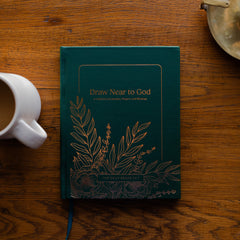 Draw Near to God Book laying on a brown wooden table next to a white coffee cup and a bronze oil lamp - Image 1 of 13