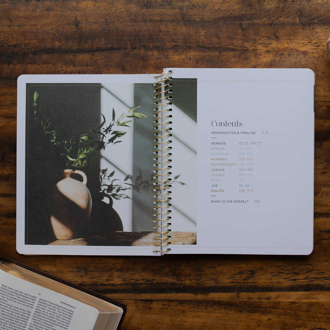 Eden to Eternity Volume 1 spiral opened to the table of contents page on a wooden table next an open bible