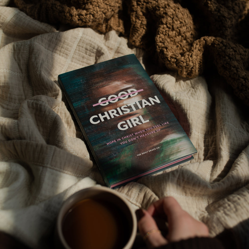 The Good Christian Girl book cover on a tan blanket near a woman's hand holding a coffee cup
