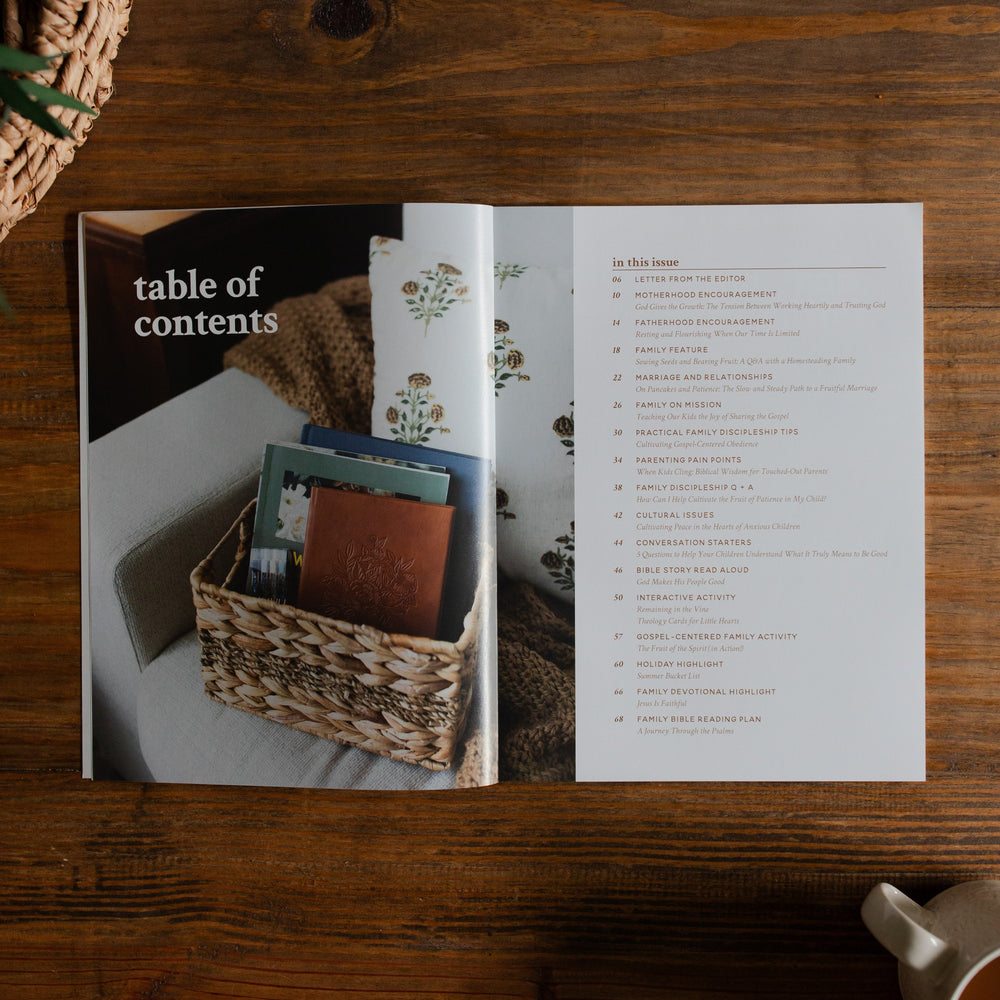 Gospel at Home Issue 8 opened to the table of contents Page on a wooden table next to a coffee cup and a woven basket