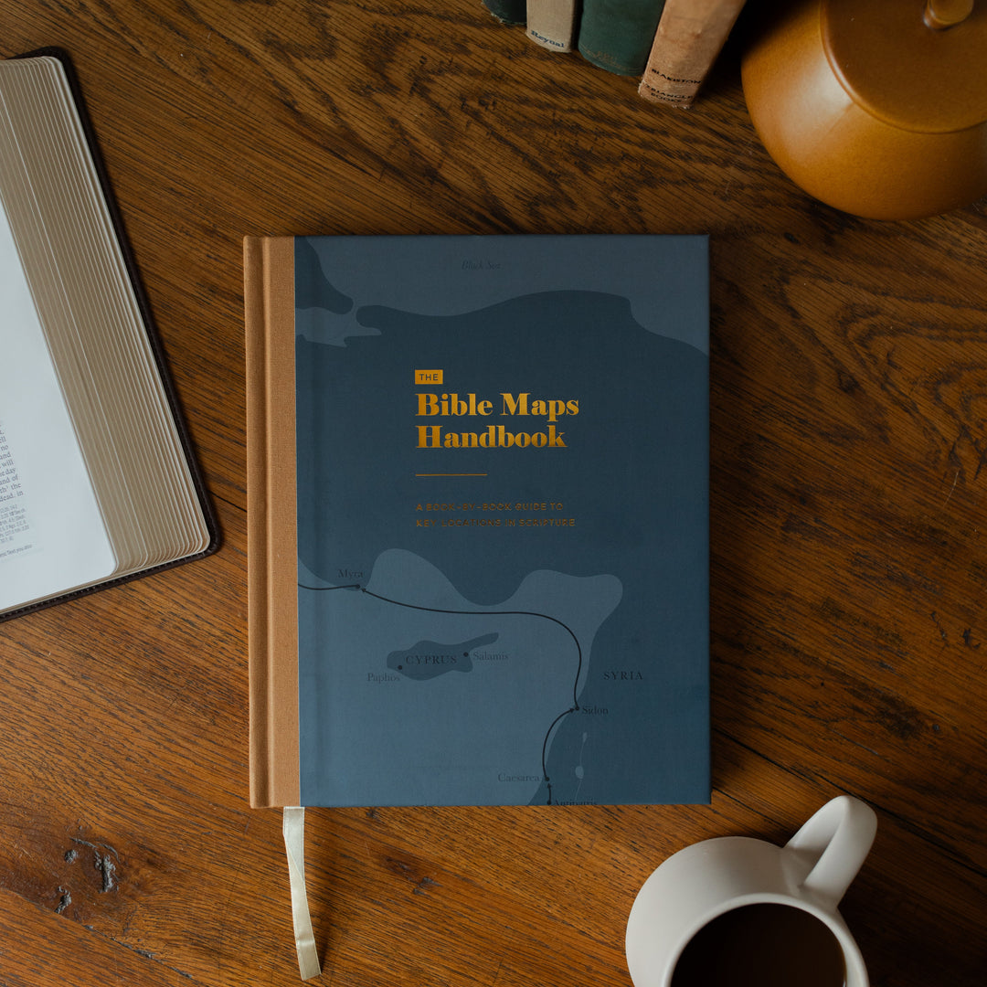The Bible Maps Handbook cover on a wooden table near an open bible and a coffee cup