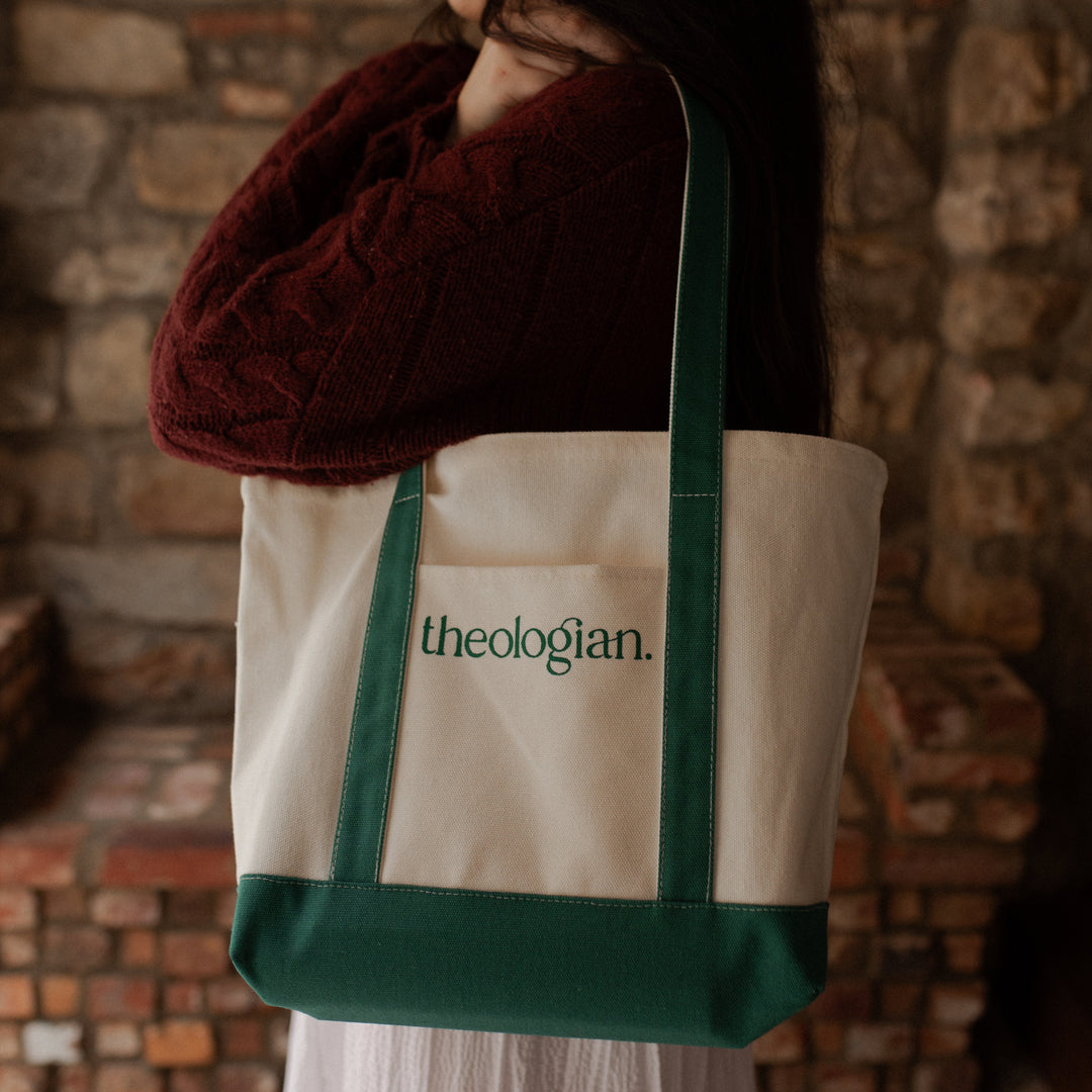 A woman with a red sweater holding a bag that says theologian on it over her shoulder
