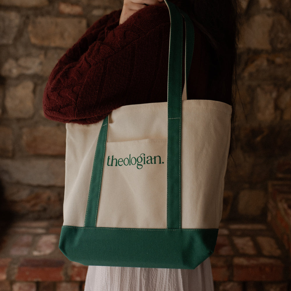 A woman with a red sweater holding a bag that says theologian on it over her shoulder while looking toward the camera direction