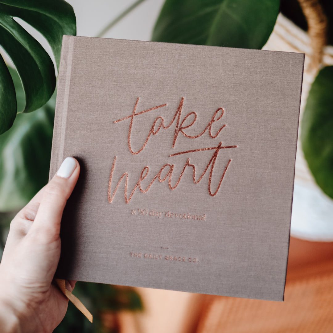 Woman holding closed Devotional book in front of a plant