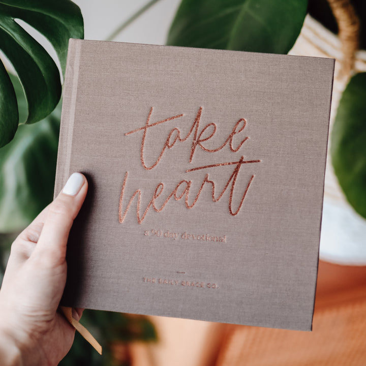 Woman holding closed Devotional book in front of a plant