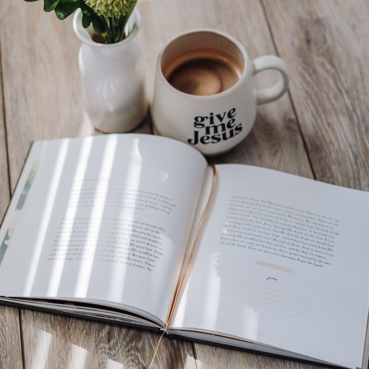 Devotional book opened next to a cup of coffee and a plant