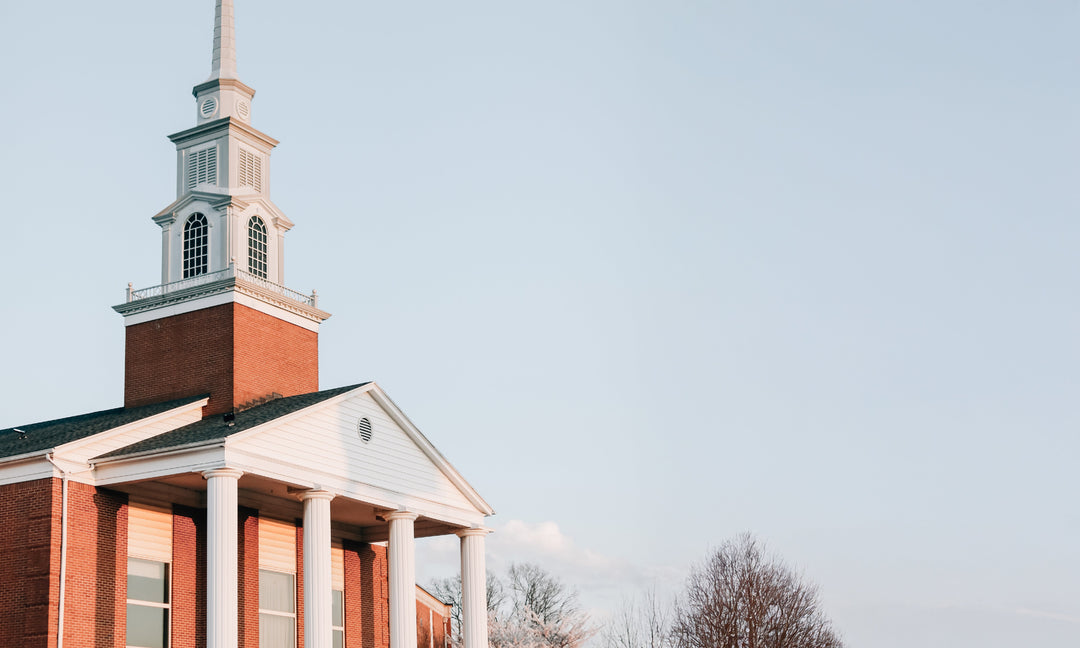 a red brick and white wood panel building with a steeple in the sunset