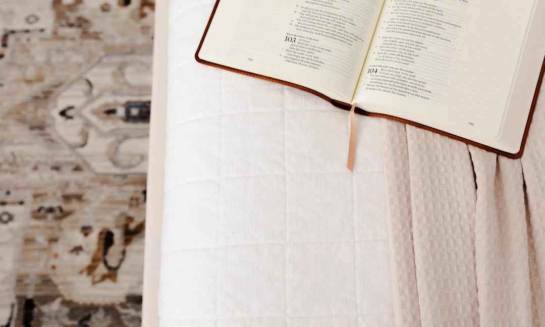 Open Bible siting on a light pink blanket and a mattress over a tan rug