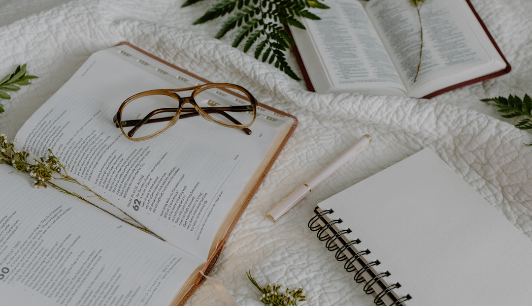 A pair of glasses on an open bible on a white blanket