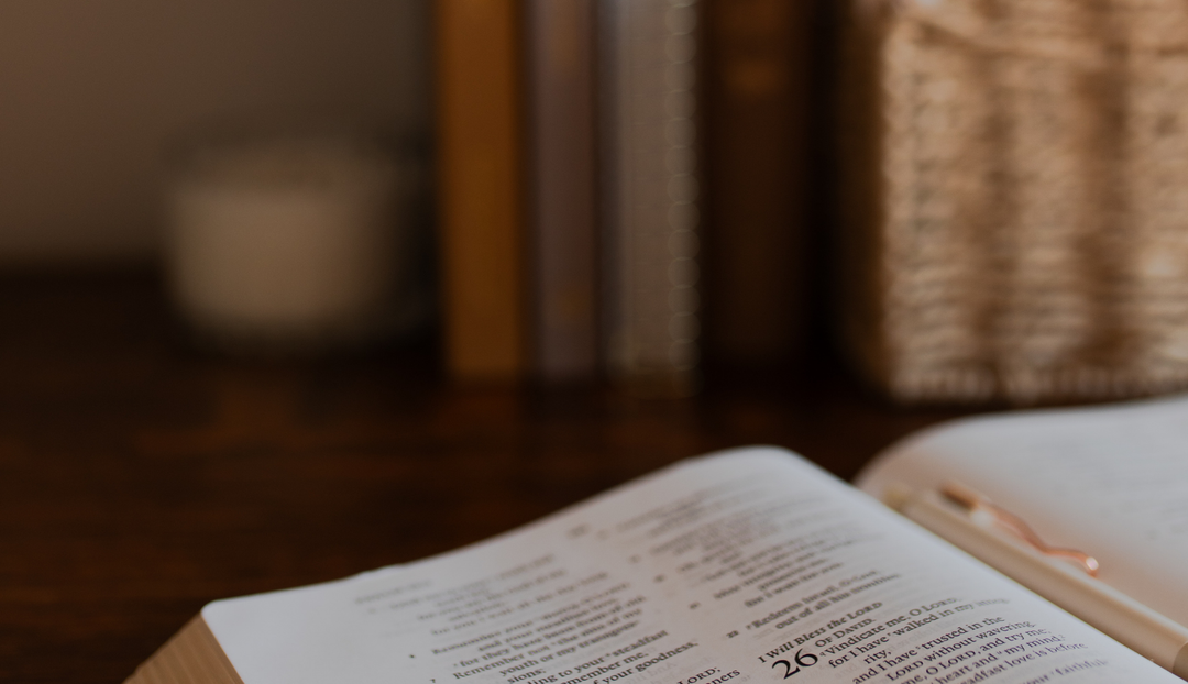 An open bible on a table near some daily grace book upright near a candle