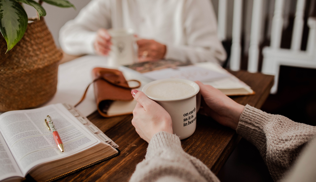 A woman holding a coffee cup on a wooden table near an open bible