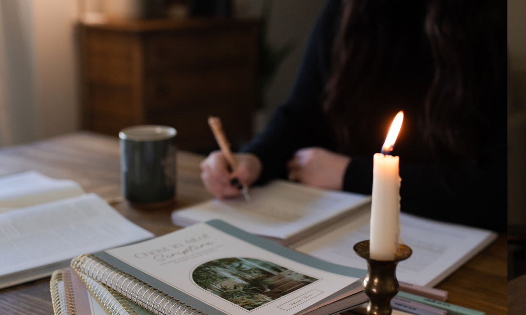 Woman writing in a journal with a Christ in all of scripture book nearby