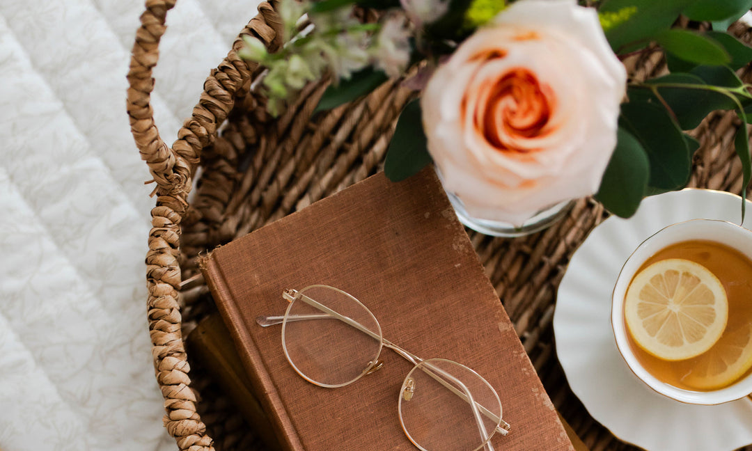 Pair of glasses on top of a book next to a cup of tea and a flower