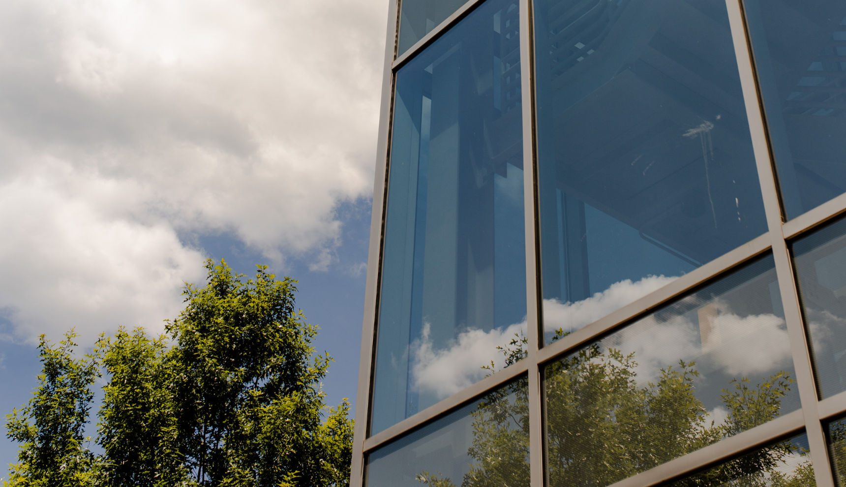 The side of a glass building near a clear and slightly cloudy sky