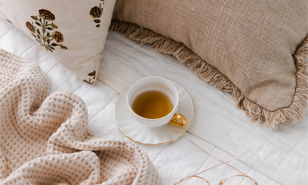 A teacup siting next to two pillows and a blanket