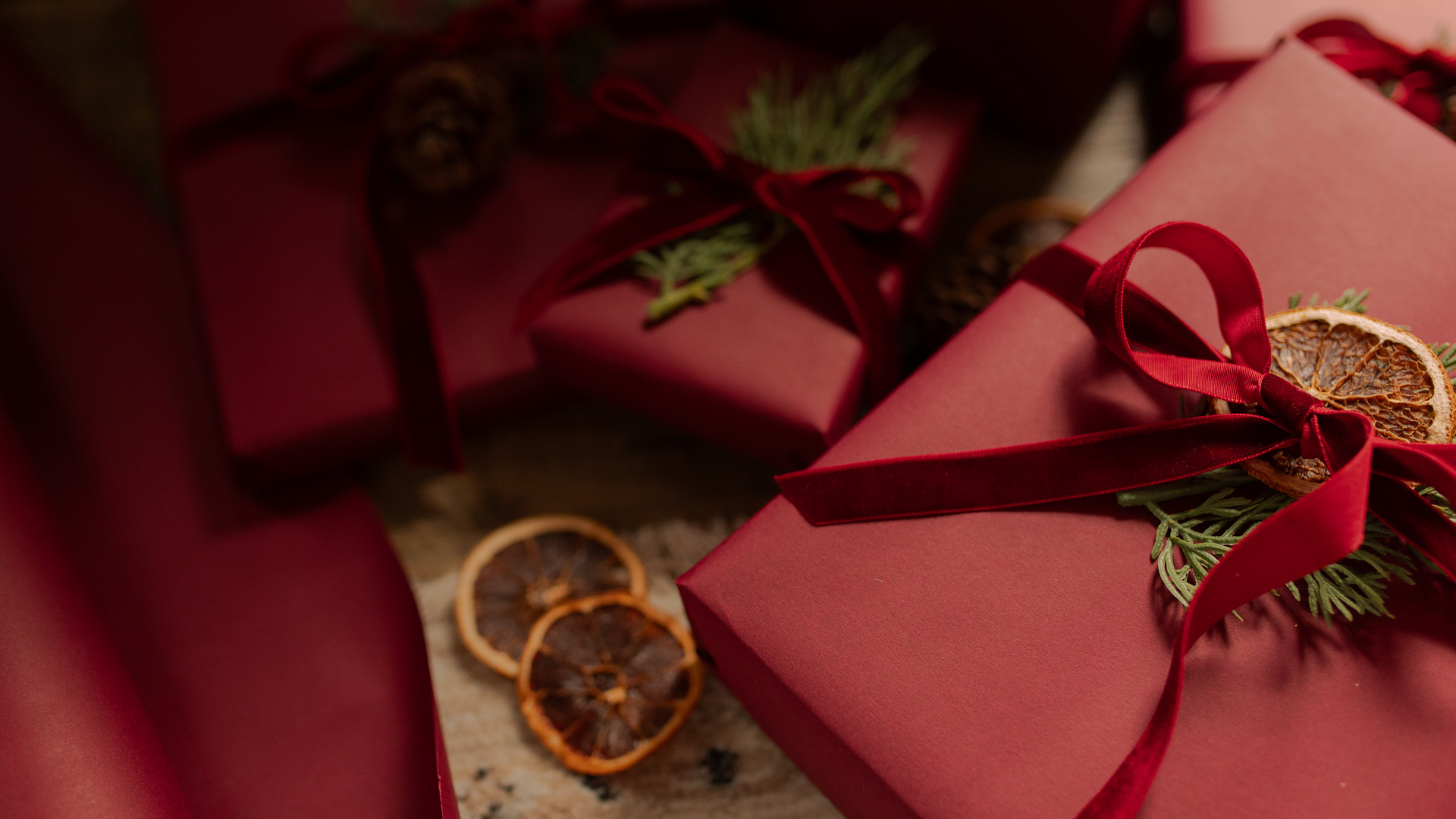 multiple gifts wrapped in red wrapping with red bows and dried orange slices