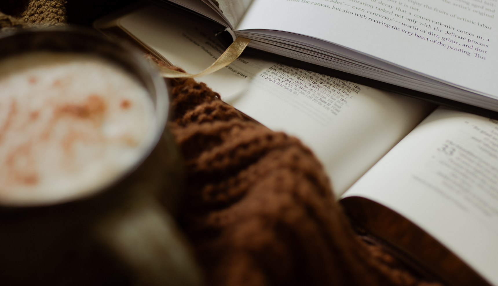 An open bible near a brown blanket and a cup of coffee with cinnamon dust