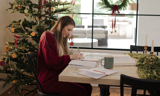 Woman writing in a journal next to a Christmas tree