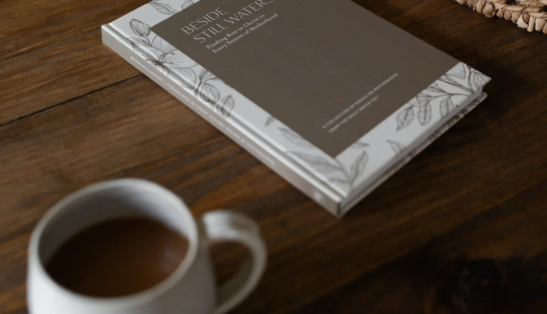 A Beside Still Waters Book on a brown wooden table next to a white coffee cup