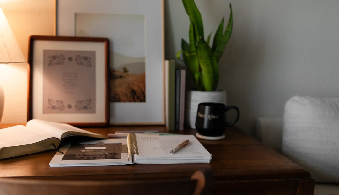 A Study resting on a brown wooden table next to a theologian mug and some prints leaning on the wall