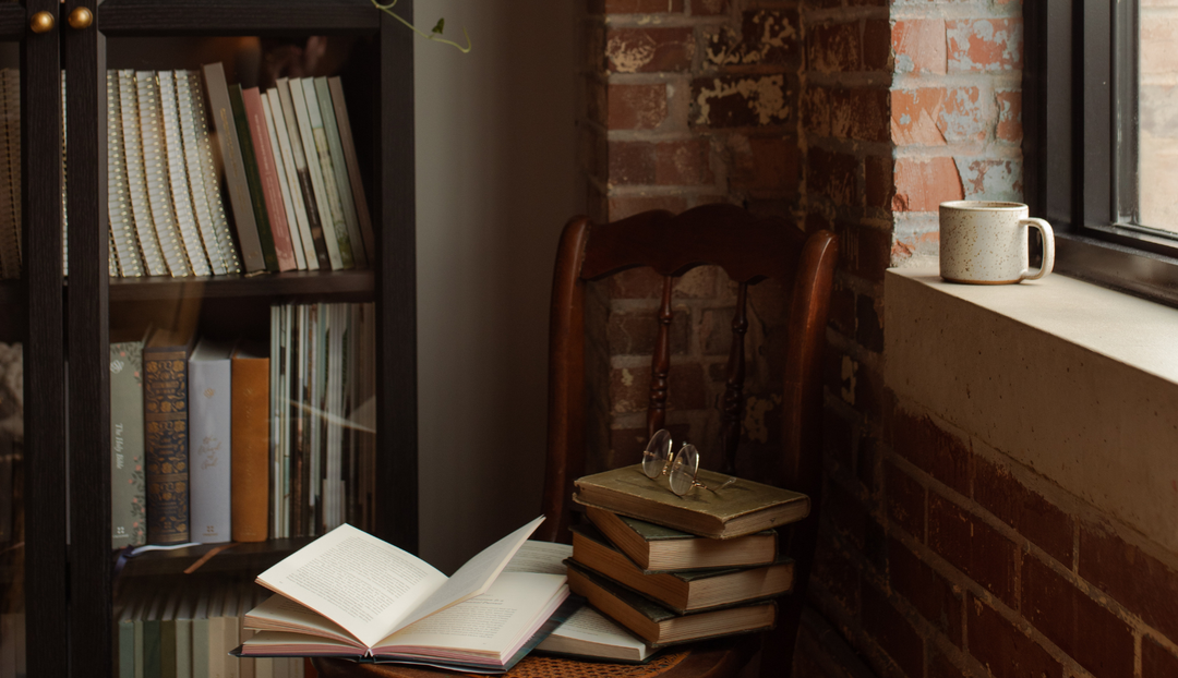 Multiple books on a table near a bookcase with multiple books and studies on it