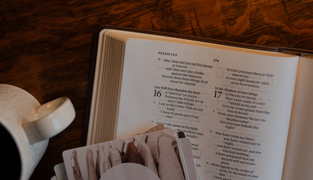 An open bible on a wooden table near a white coffee cup